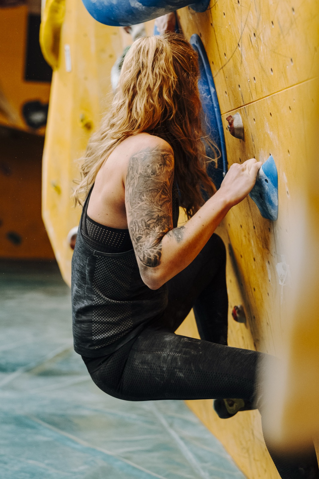 Kletterin an der gelben Wand greift nach einem blauen Griff
