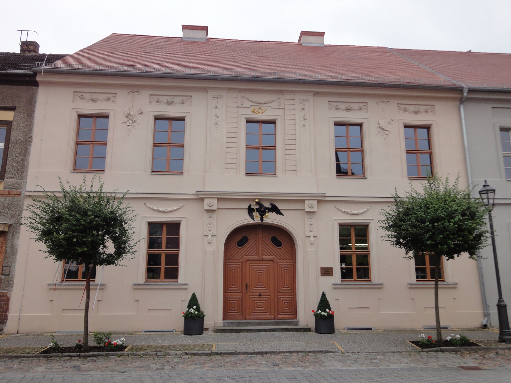 Die Alte Posthalterei in Beelitz von der Straße aus – klassizistische Fassade mit Posthorn und preußischem Adler über dem Portal