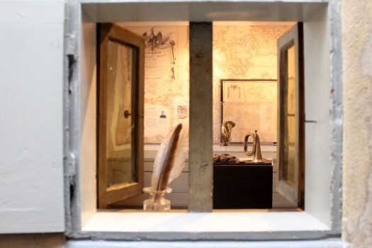 Blick durch ein Fenster in die Ausstellung mit Federkiel, Posthorn und alten Karten