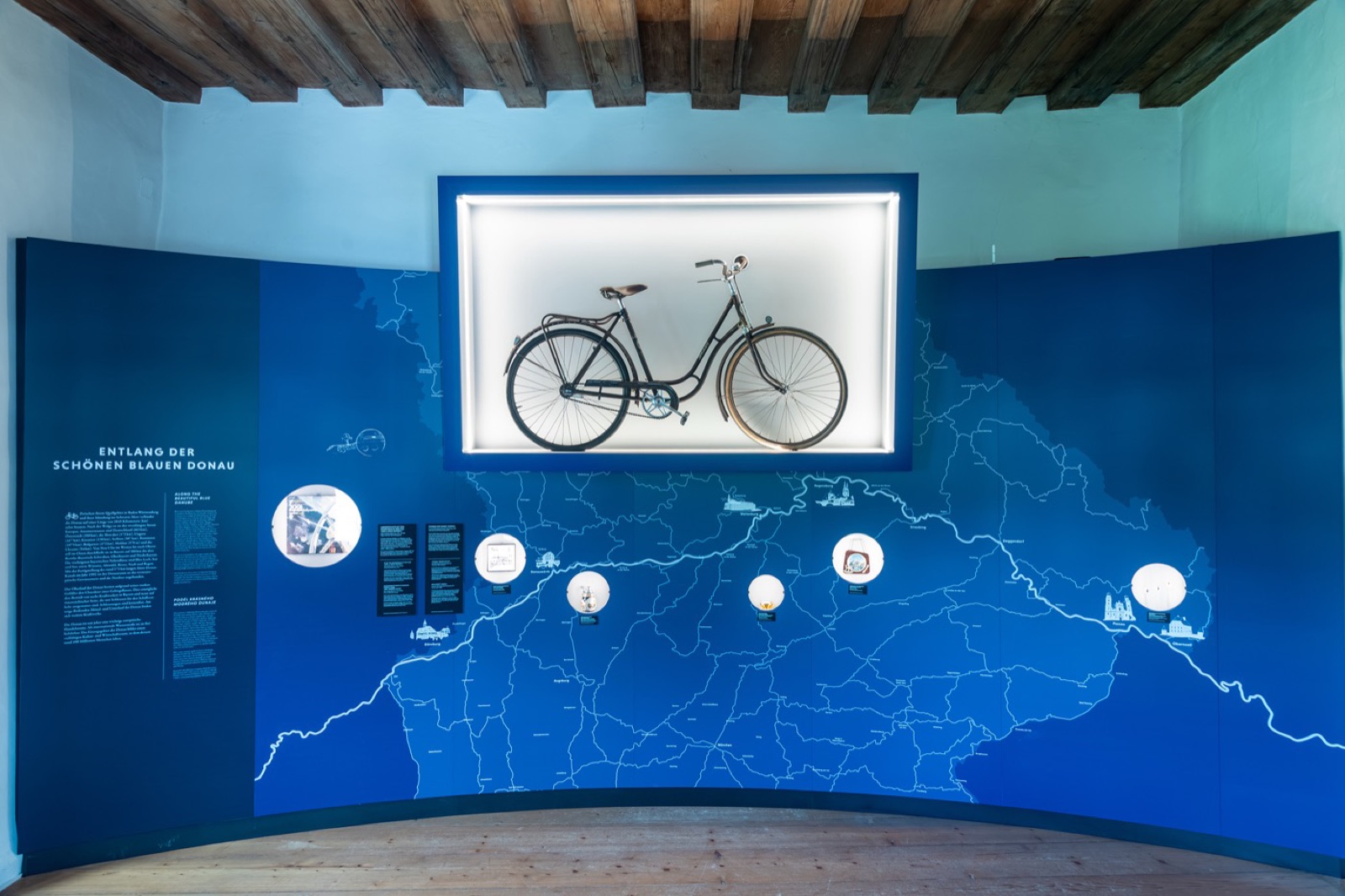 Blaue Wandkarte des Donaulaufs mit einem historischen Fahrrad in einer beleuchteten Nische