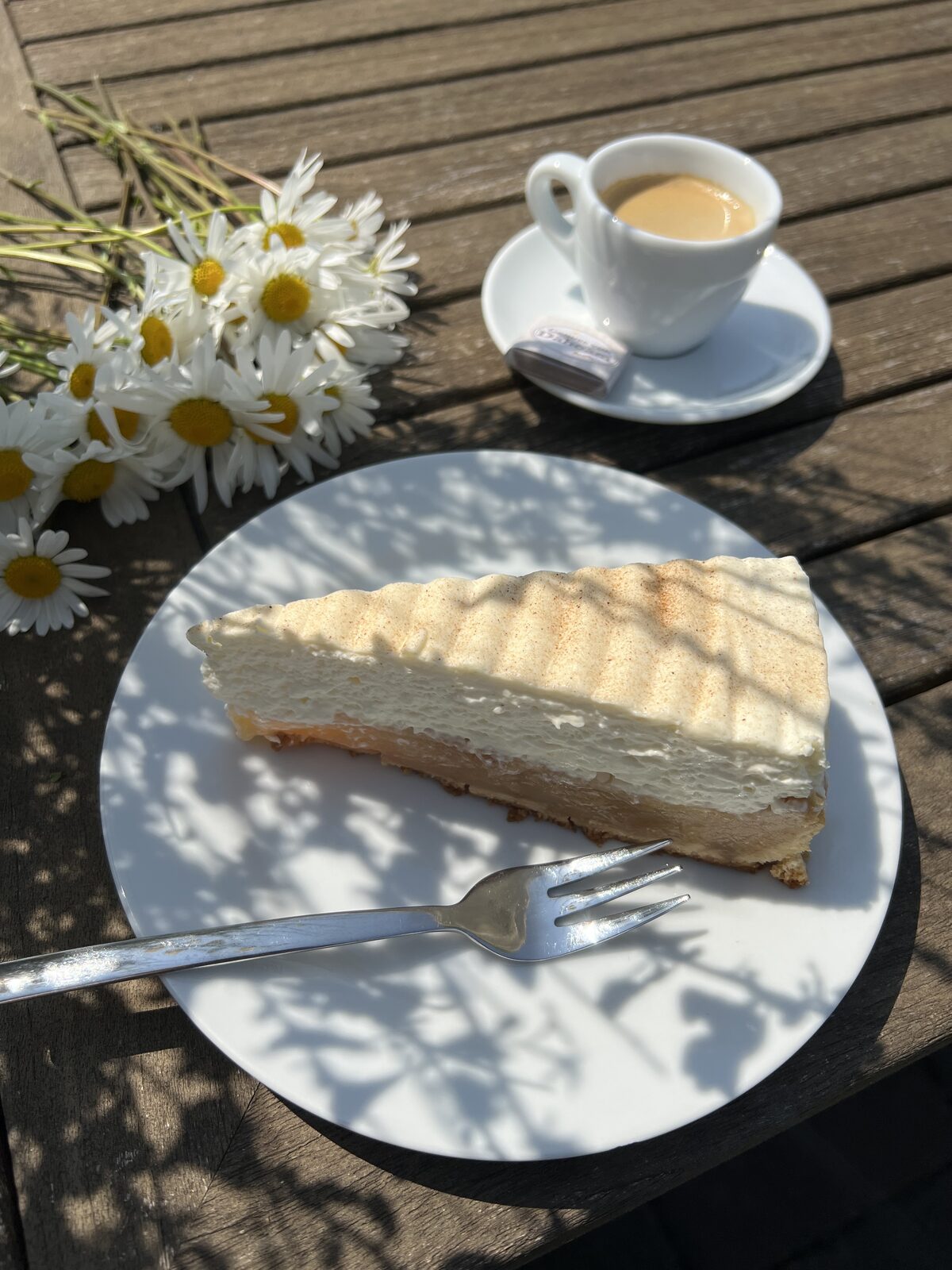 Stück Käsesahnetorte mit Espresso auf einem Tisch im Freien