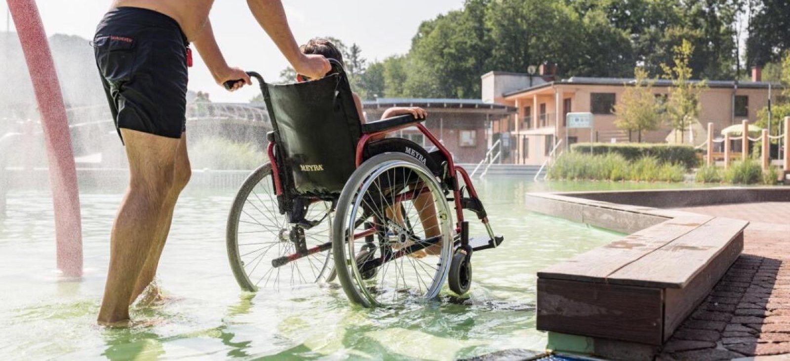 Ein Wasserrollstuhl wird über den flachen Beckeneinstieg ins Wasser geschoben