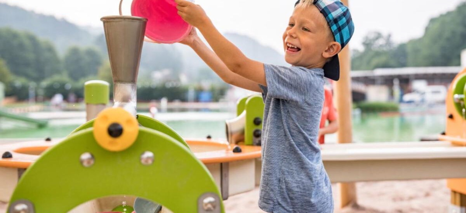 Ein Kind schüttet Wasser in eine Wasserspielanlage am Sandspielplatz