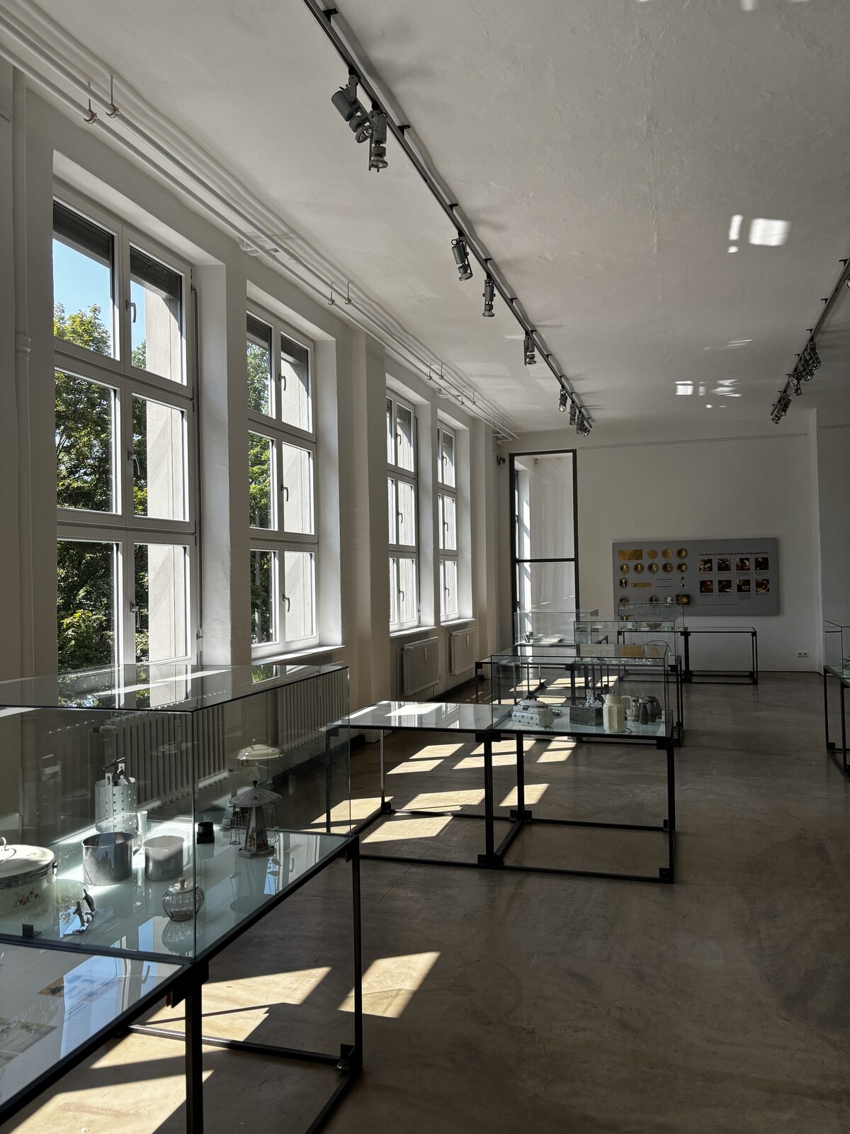 Ausstellungsraum mit Glasvitrinen voller Metallwaren an hohen Sprossenfenstern