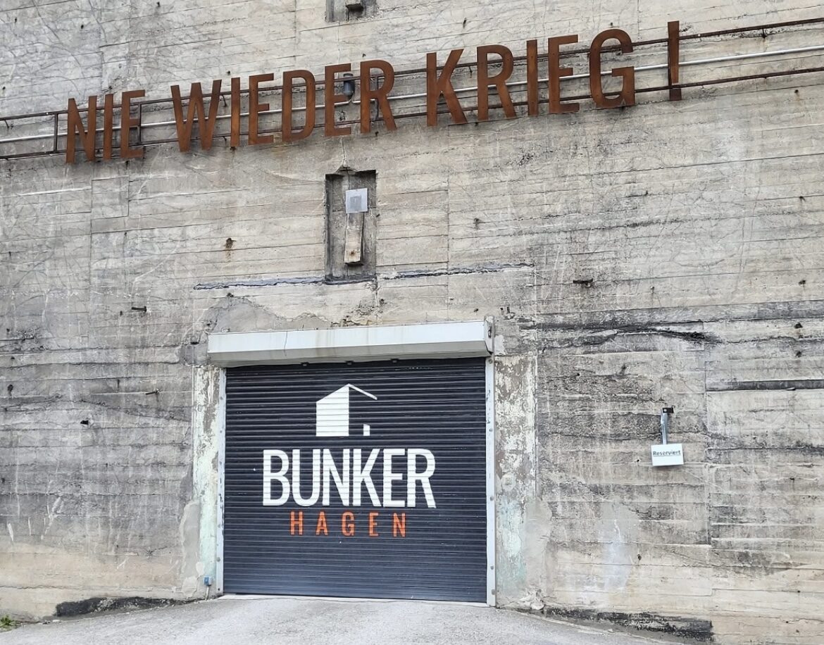Bunkereingang mit dem rostigen Schriftzug „Nie wieder Krieg!“ über dem Tor