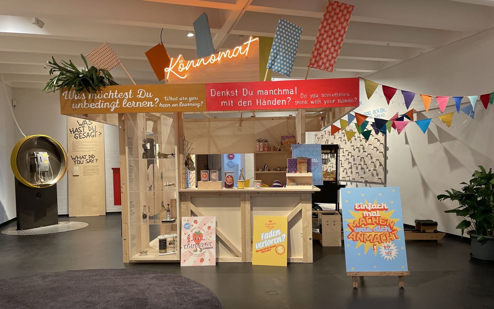 Mitmachstation „Könnomat“ im Kindermuseum mit bunten Wimpeln und Fragen an der Wand