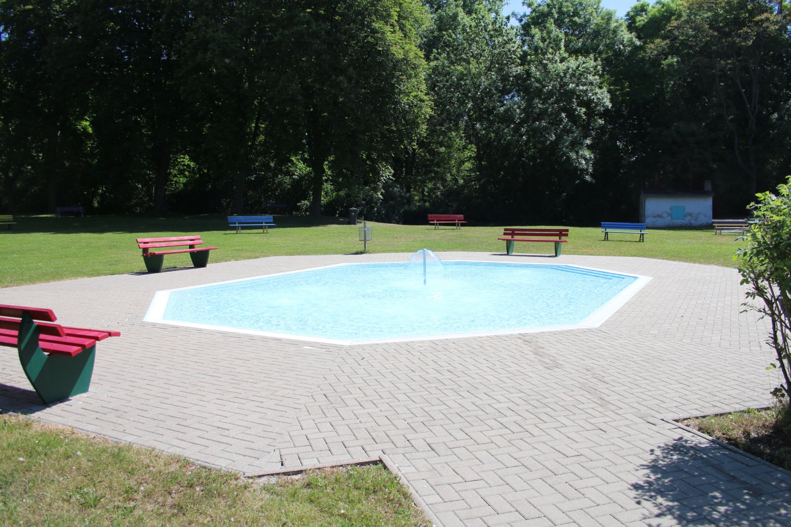 Planschbecken mit Wasserpilz, umgeben von Bänken und Liegewiese