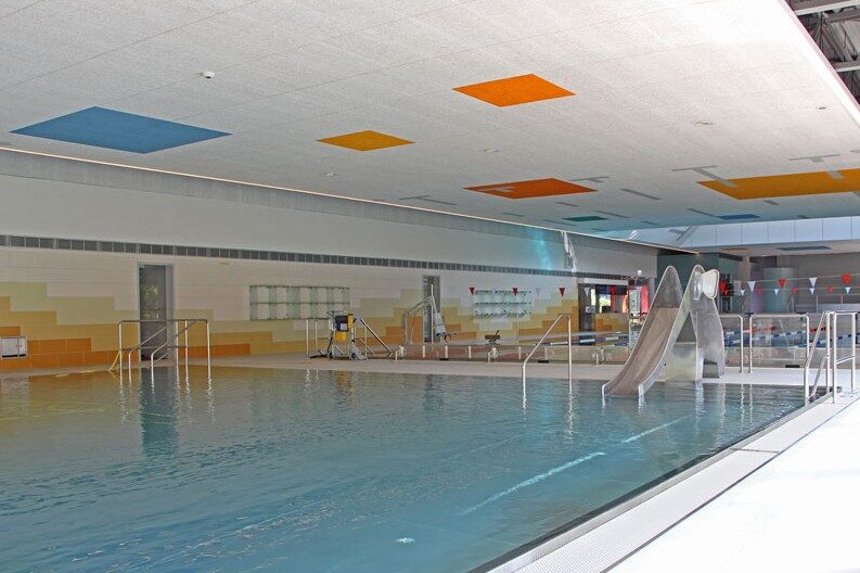 Schwimmerbecken mit Rutsche unter farbigen Deckenfeldern