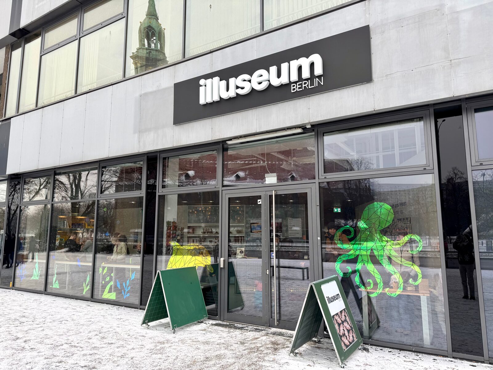 Eingang des Illuseum Berlin mit Schriftzug und grünem Tintenfisch an der Scheibe