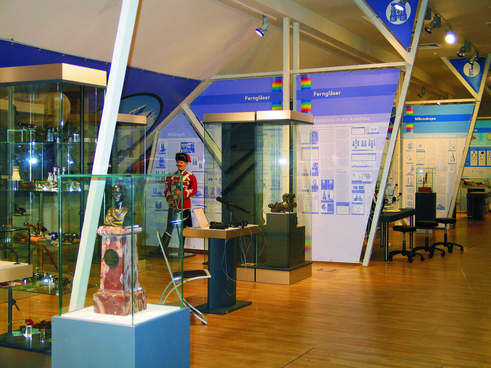 Ausstellungshalle mit Vitrinen voller Ferngläser und Mikroskope, im Vordergrund eine Büste