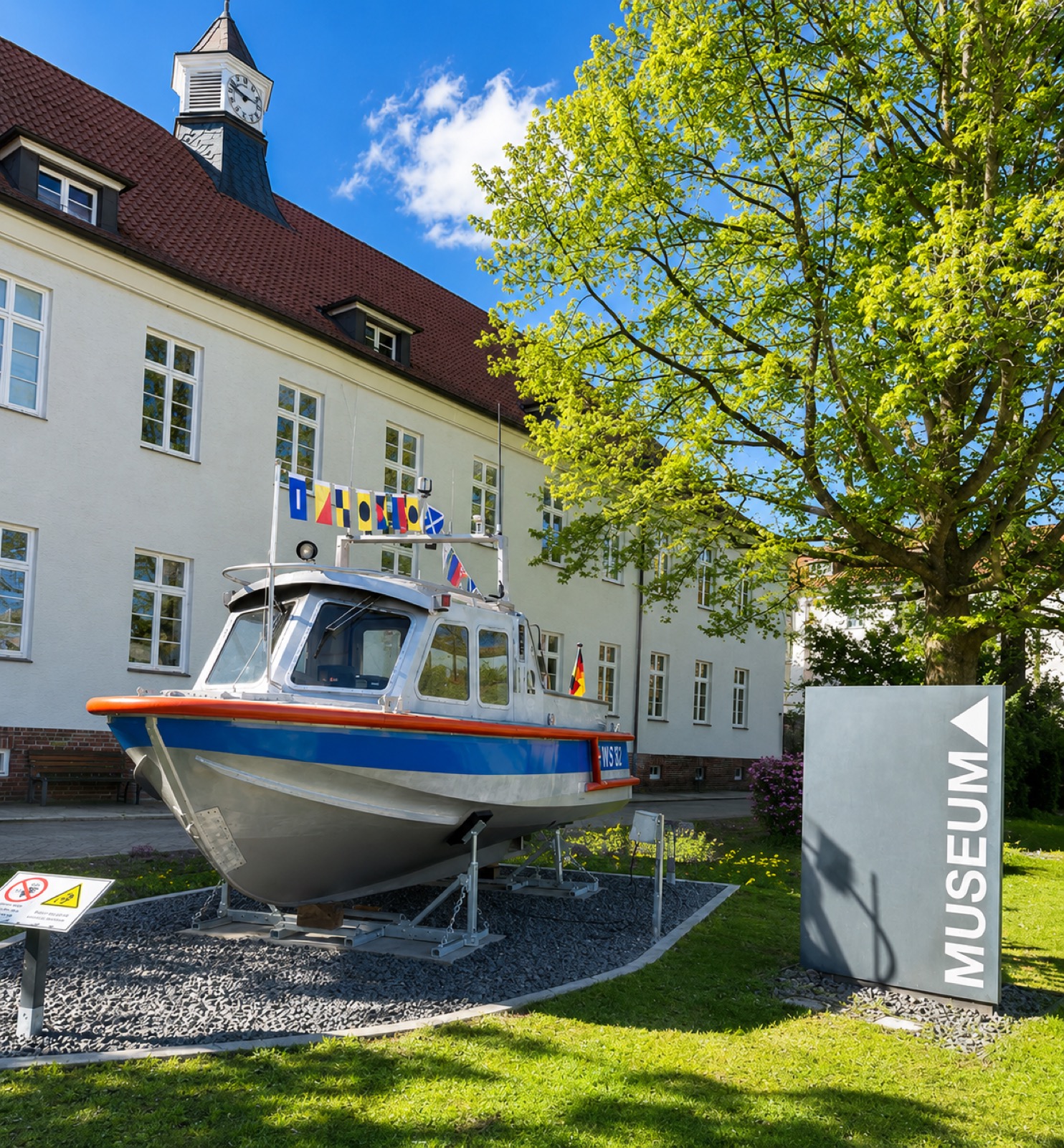 Blau-weißes Polizeiboot auf einem Gestell vor dem Museumsgebäude, daneben ein Schild mit der Aufschrift Museum